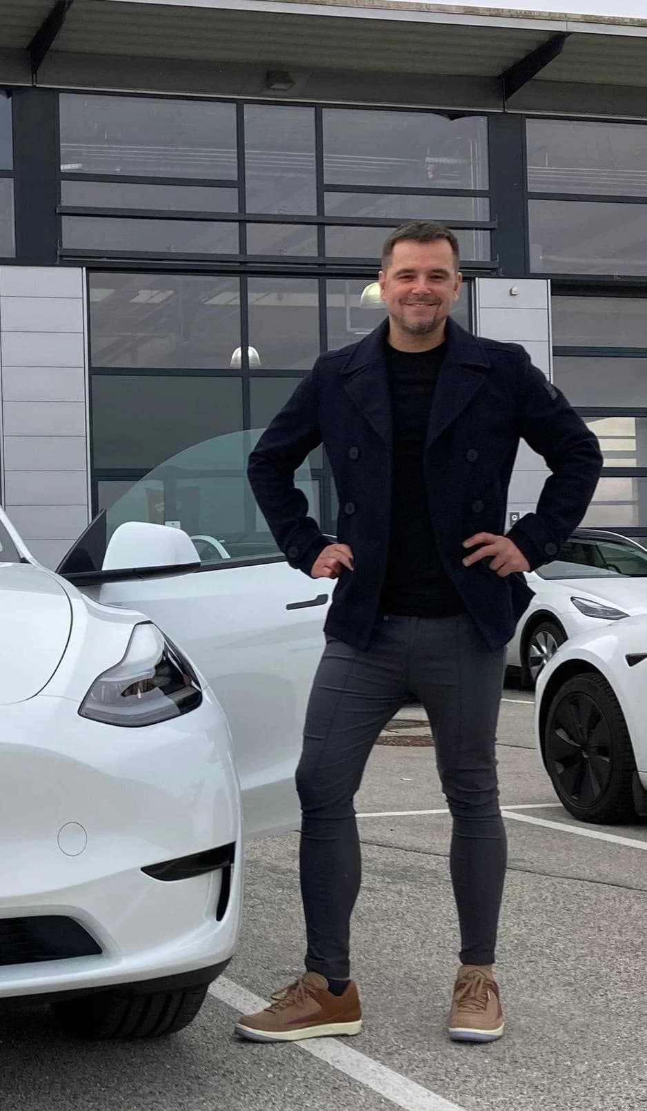 ein foto des ceos: David Wieser, Gründer von KIWebBoost, steht mit einem Lächeln vor seinem frisch gekauften Tesla Model Y. Die Fahrertür ist geöffnet, und im Hintergrund ist ein modernes Gebäude mit Glasfassade zu sehen. David Wieser CEO, KIWebboost